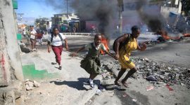 Seorang wanita dengan putrinya berjalan melewati barikade yang dipasang oleh anggota polisi saat demonstrasi pecah di Port-au-Prince, (AP PHOTO/ODELYN JOSEPH)